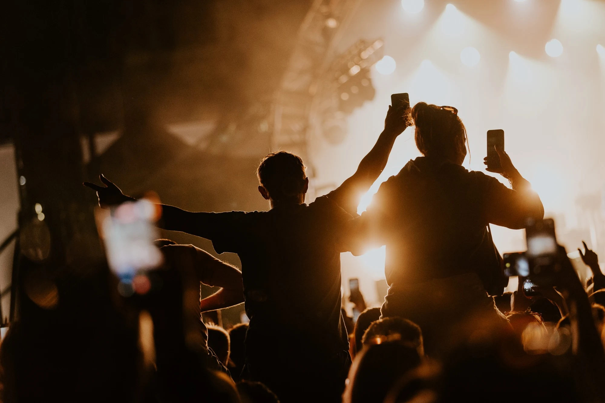 Fans raising their phones beneath golden concert lights at Ebrington Square